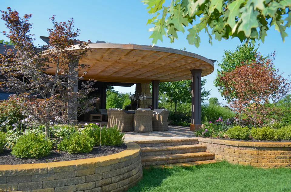 Backyard pavilion with curved roof, stone steps, retaining walls, and planting